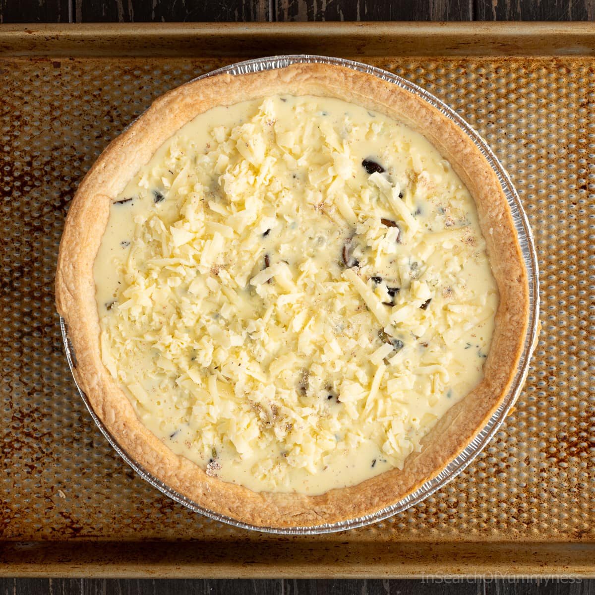 Egg and cream mixture for quiche in pie shell, topped with more grated cheddar cheese.