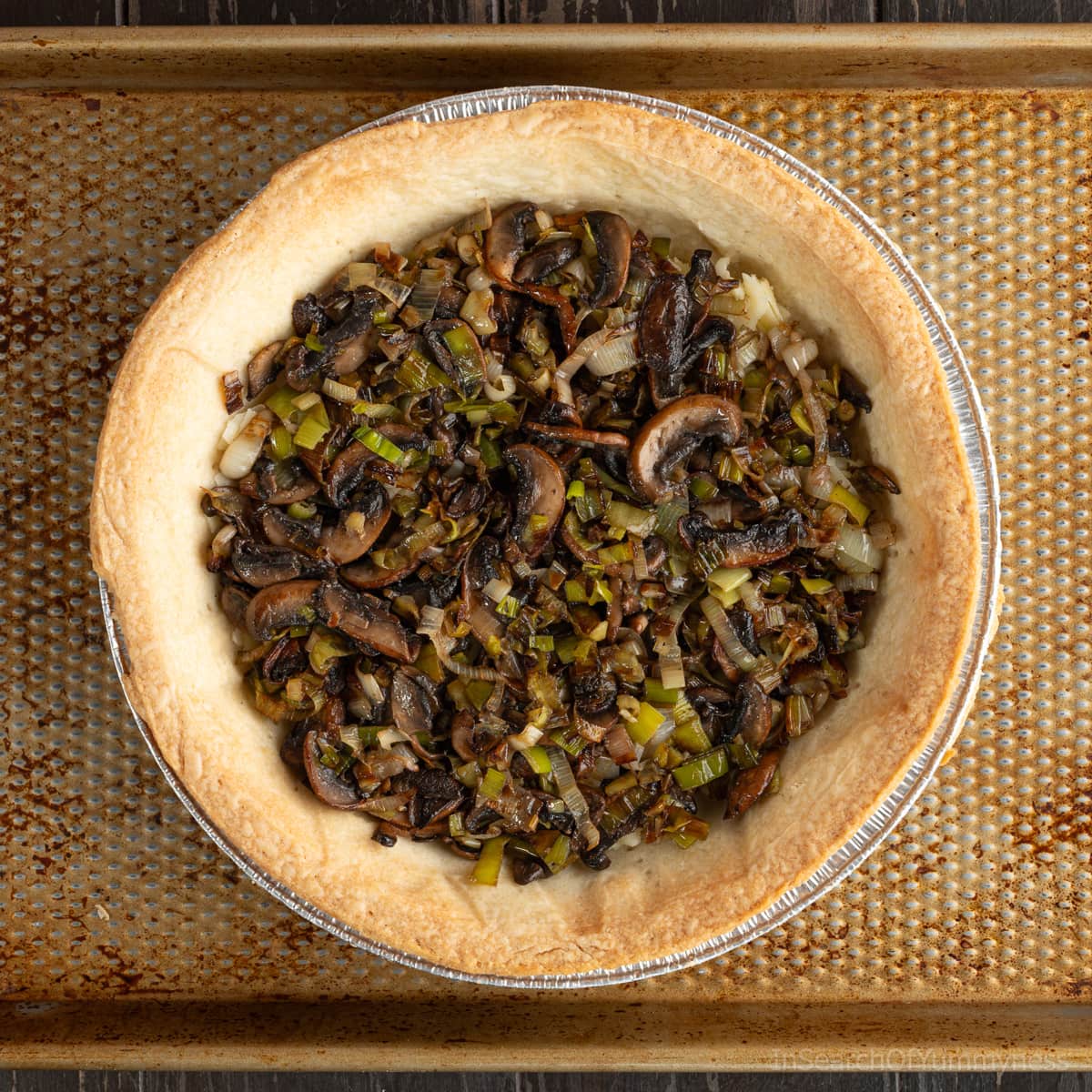 A baked pie shell filled with shredded cheddar cheese, and sauted leeks and mushrooms.