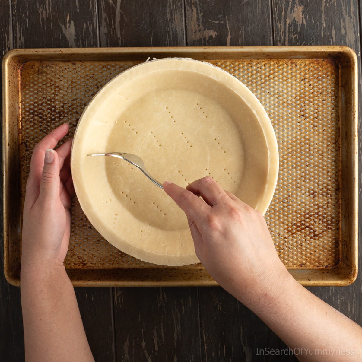 Someone using a fork to poke holes into a pre-made deep dish pie shell.