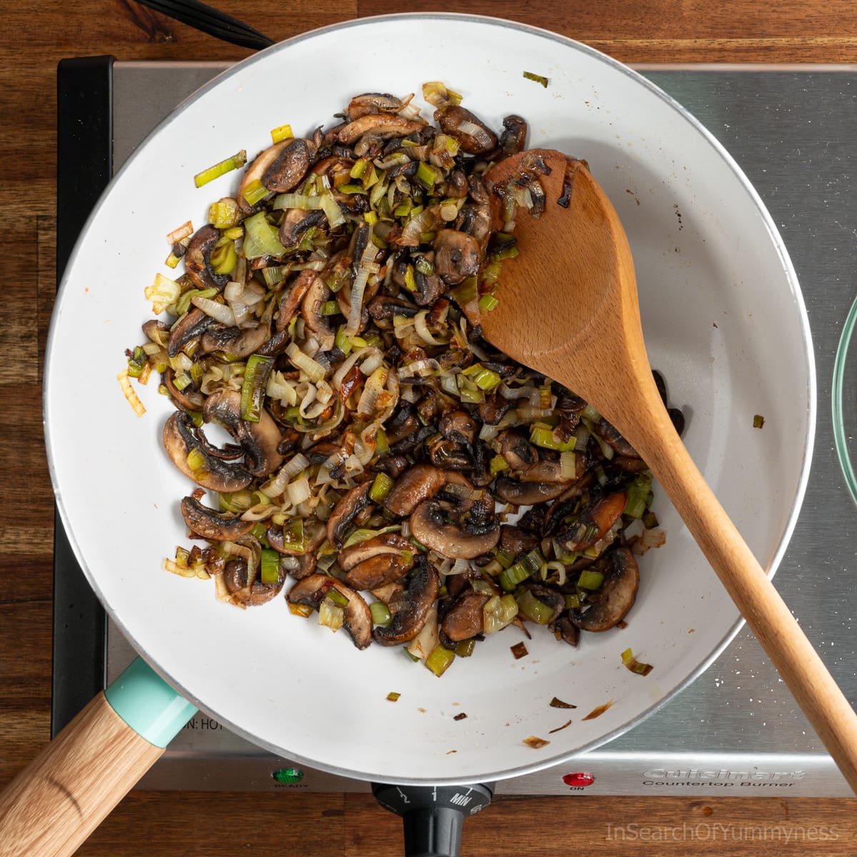 A non-stick skillet with sautéd leeks and mushrooms on a portable electric stovetop.