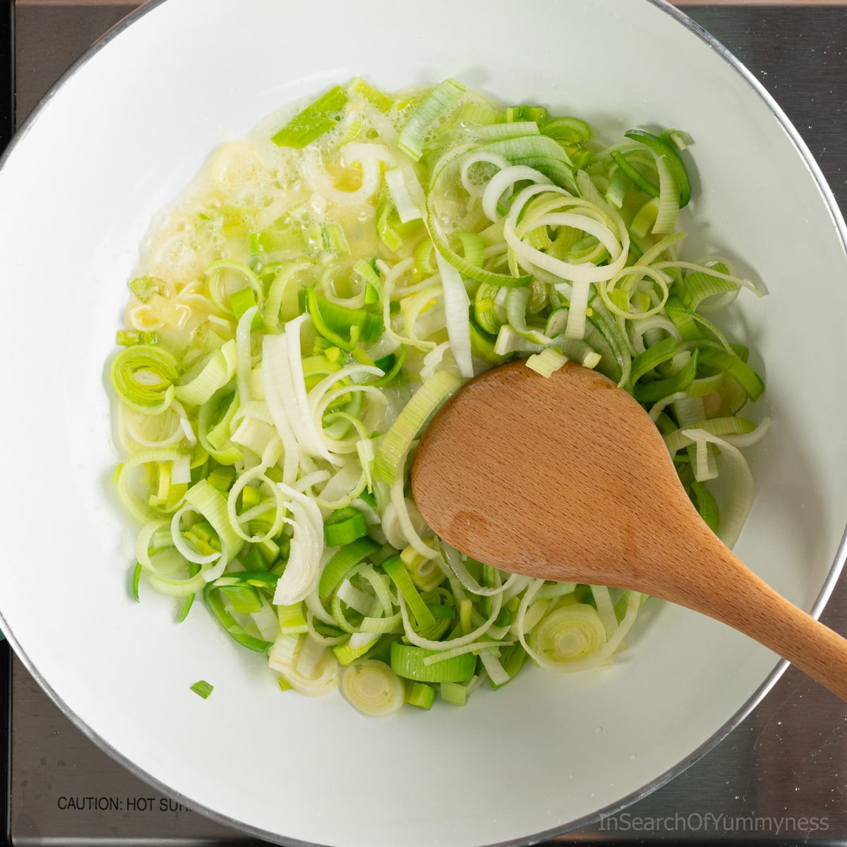 Sautéing leeks in butter in a frying pan. There is a wooden spoon in the pan as well.