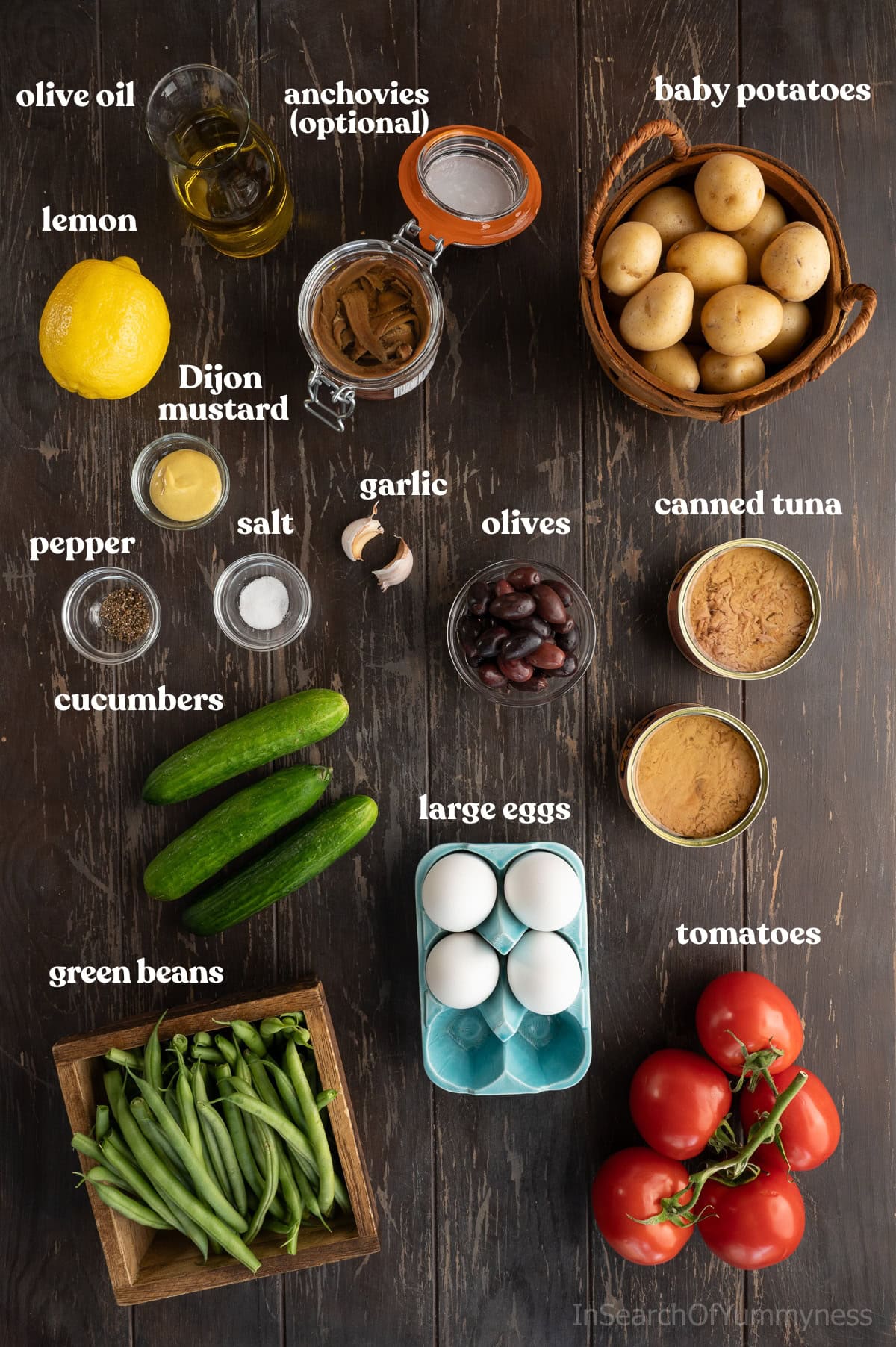 Ingredients needed to make a non-traditional tuna nicoise salad with potatoes laid out on a wooden table.