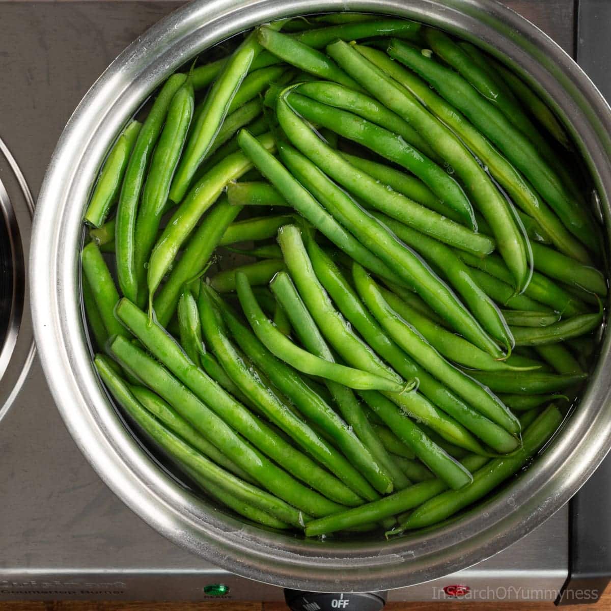 Fresh green beans cooking in a saucepan on the stovetop.