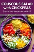 A bowl of couscous salad with chickpeas, tomato wedges, and diced vegetables next to a wooden spoon on a purple napkin. There is another bowl of couscous on the top right. Text overlay says "Couscous Salad with Chickpeas. Easy No-Stove Cooking Method.