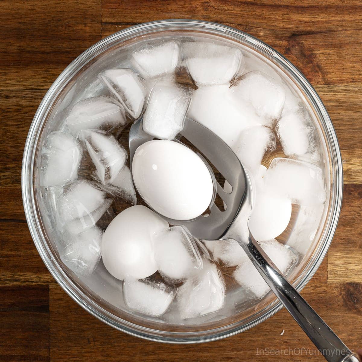 A slotted spoon placing a boiled egg into a bowl of ice water to cool down.