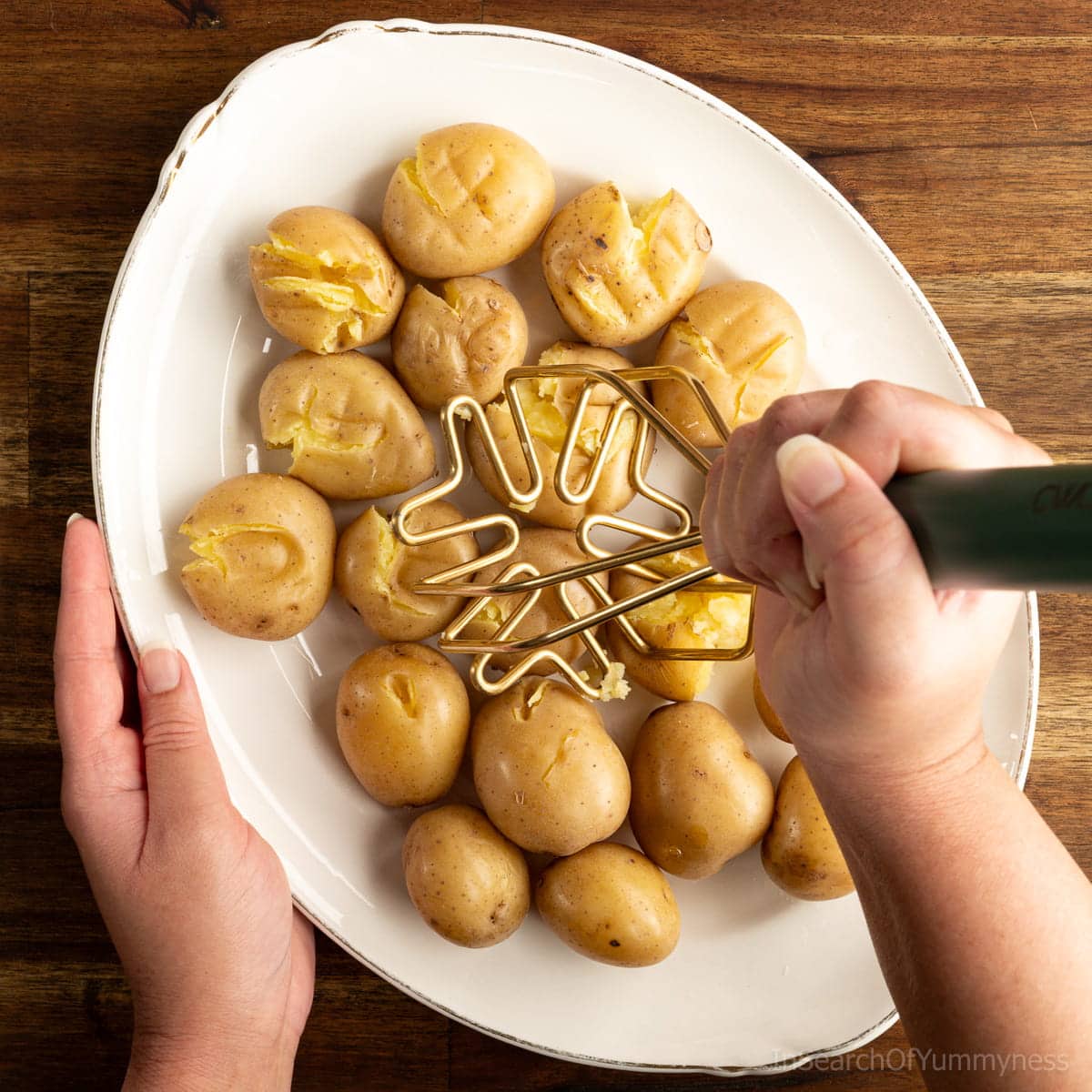 Using a potato masher to press down on boiled new potatoes until they crack.