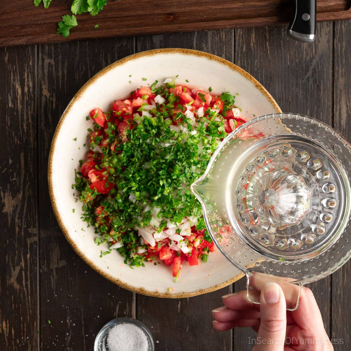 Using an old fashioned glass citrus reamer to add lime juice to a large bowl with finely diced tomatoes, onion, serrano peppers and chopped cilantro.