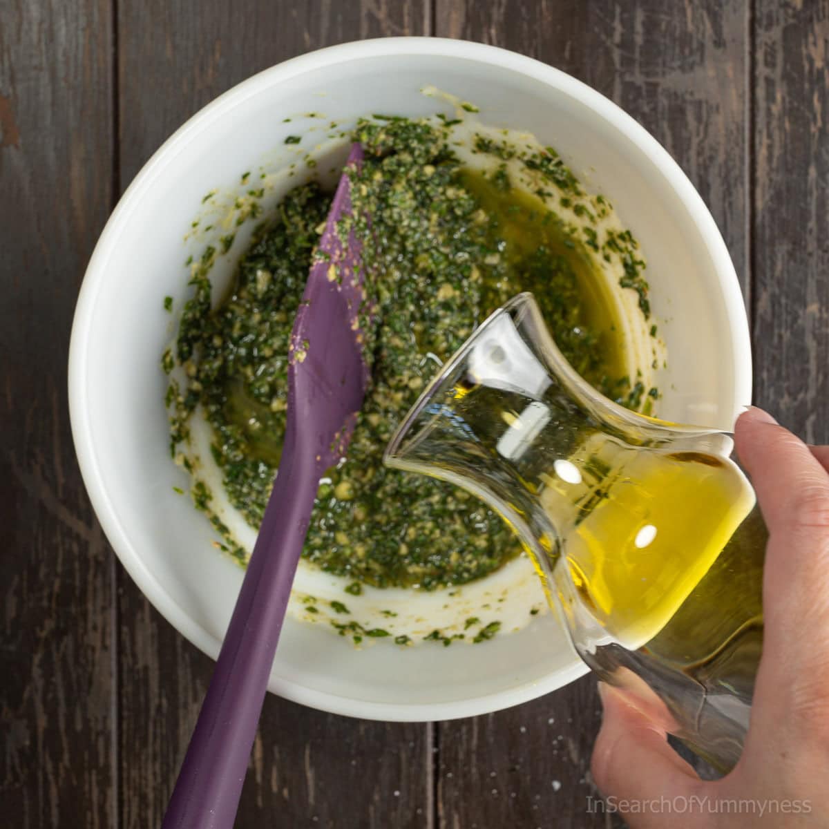 Pouring the remaining oil into a bowl with freshly blended walnut basil pesto.