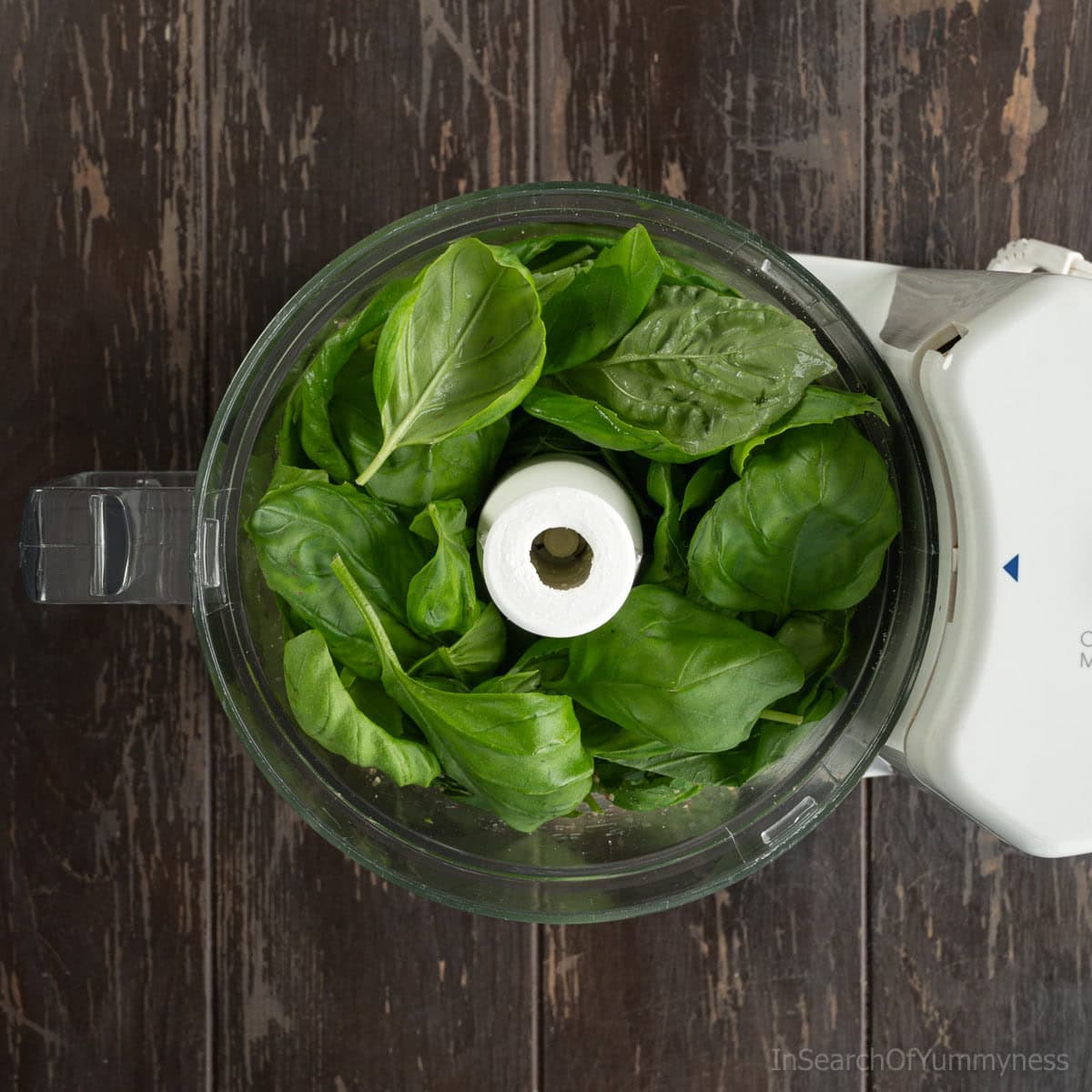 Adding fresh green basil leaves to the food processor with chopped walnuts.