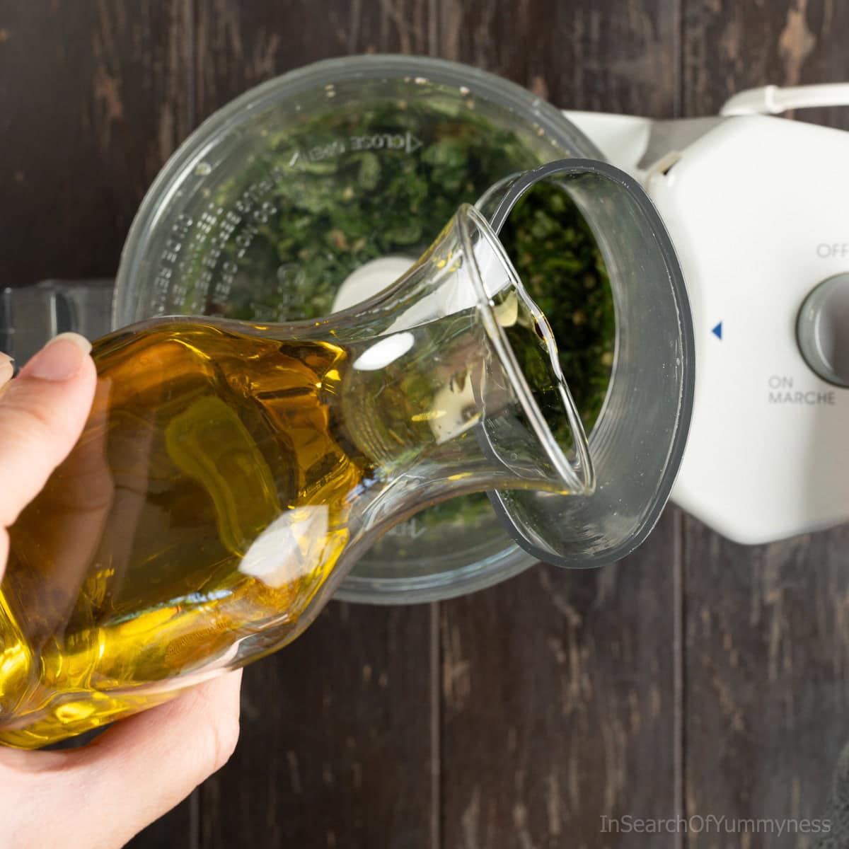 Drizzling extra virgin olive oil into a food processor while blending basil pesto.