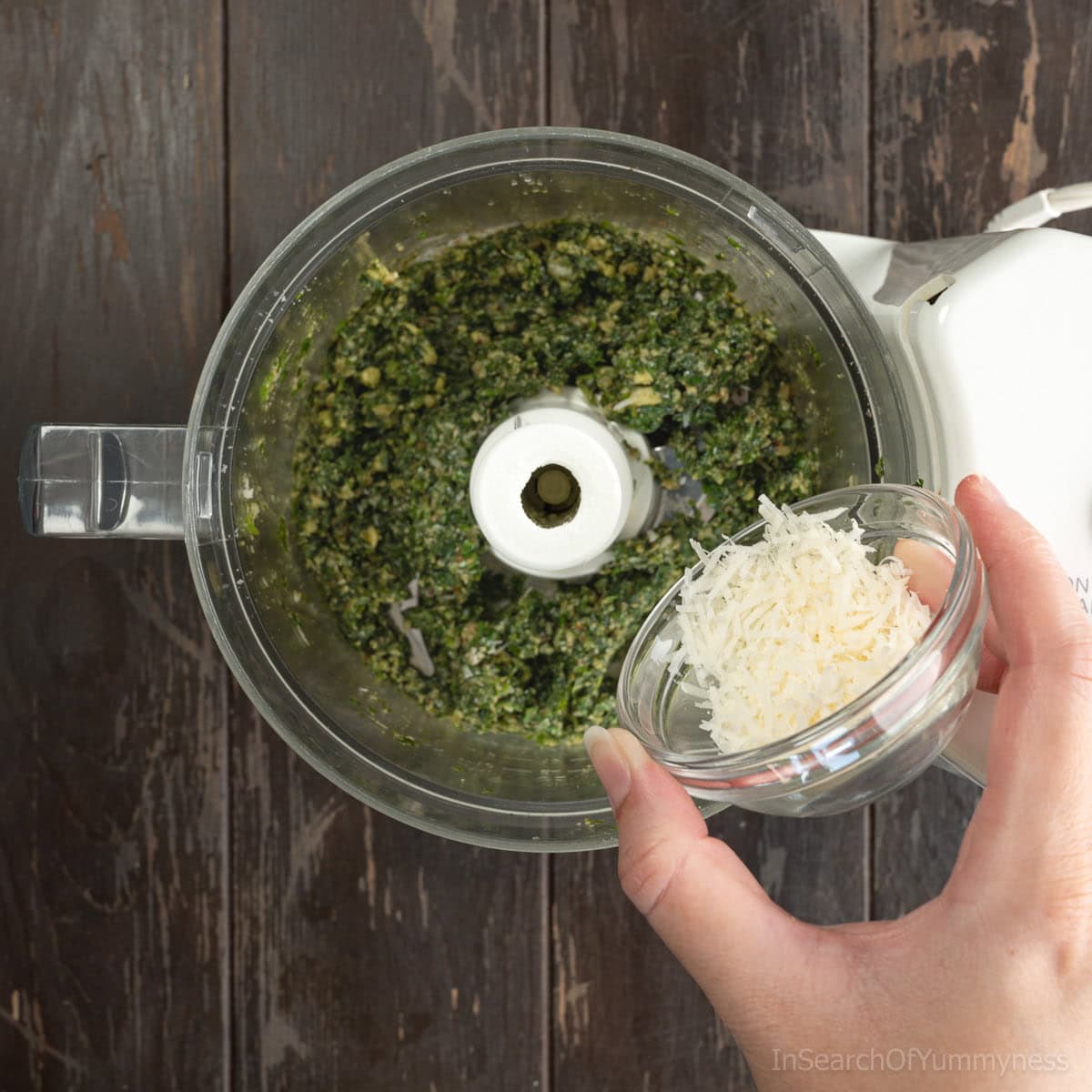 Pouring freshly grated parmesan cheese into the blended walnut basil pesto.