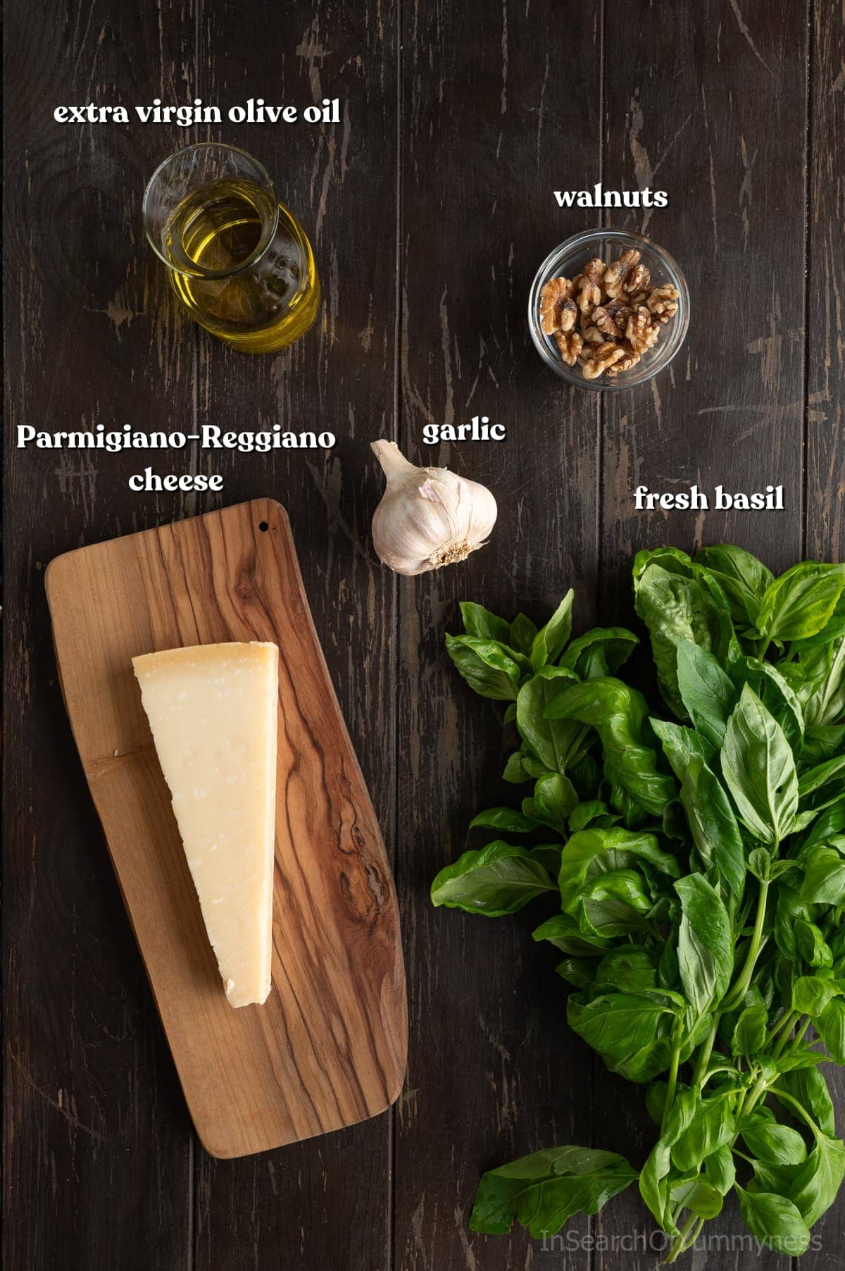 Ingredients to make basil pesto with walnuts, including olive oil, walnuts, garlic, basil and Parmigiano-Reggiano cheese, on a dark wooden table.