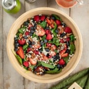 A wooden bowl full of baby spinach, fresh berries, goat cheese crumbles and toasted pecans.