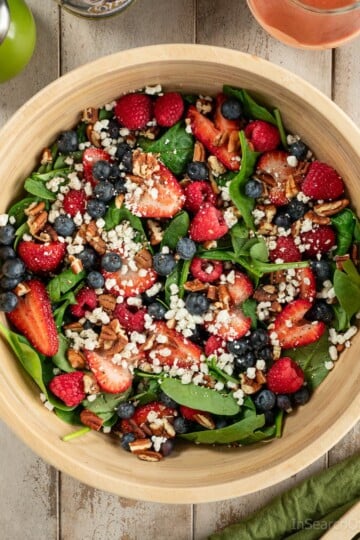 A wooden bowl full of baby spinach, fresh berries, goat cheese crumbles and toasted pecans.