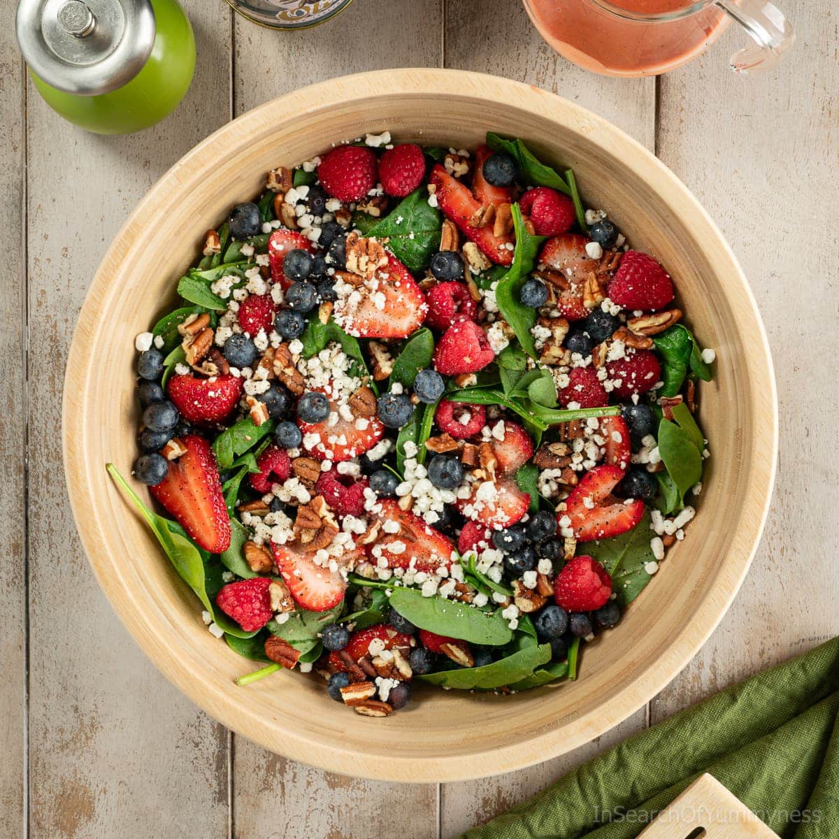 A wooden bowl full of baby spinach, fresh berries, goat cheese crumbles and toasted pecans.