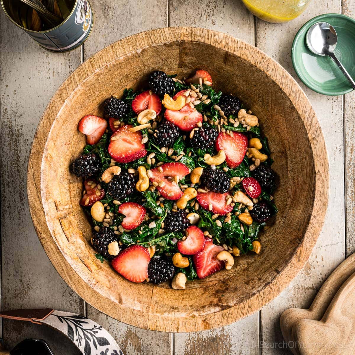 A large wooden bowl full of summer kale salad with strawberries, blackberries, sunflower seeds and cashews.