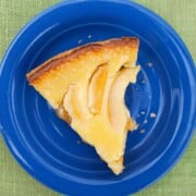 A slice of freshly baked sour cream peach pie on a blue plate, on a green tablecloth.