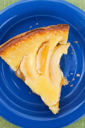A slice of freshly baked sour cream peach pie on a blue plate, on a green tablecloth.