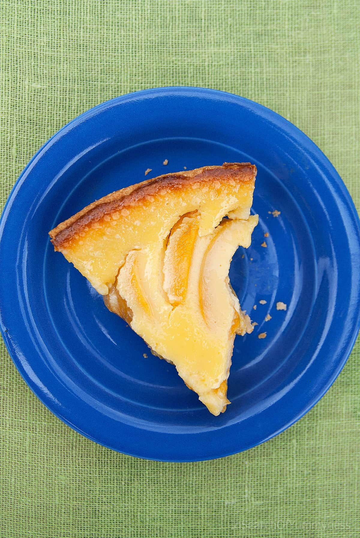 A slice of freshly baked sour cream peach pie on a blue plate, on a green tablecloth.