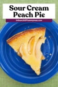 Vertical Pinterest graphic featuring a slice of freshly baked sour cream peach pie on a blue plate, on a green tablecloth. The text overlay says "Sour Cream Peach Pie. InSearchOfYummyness.com".