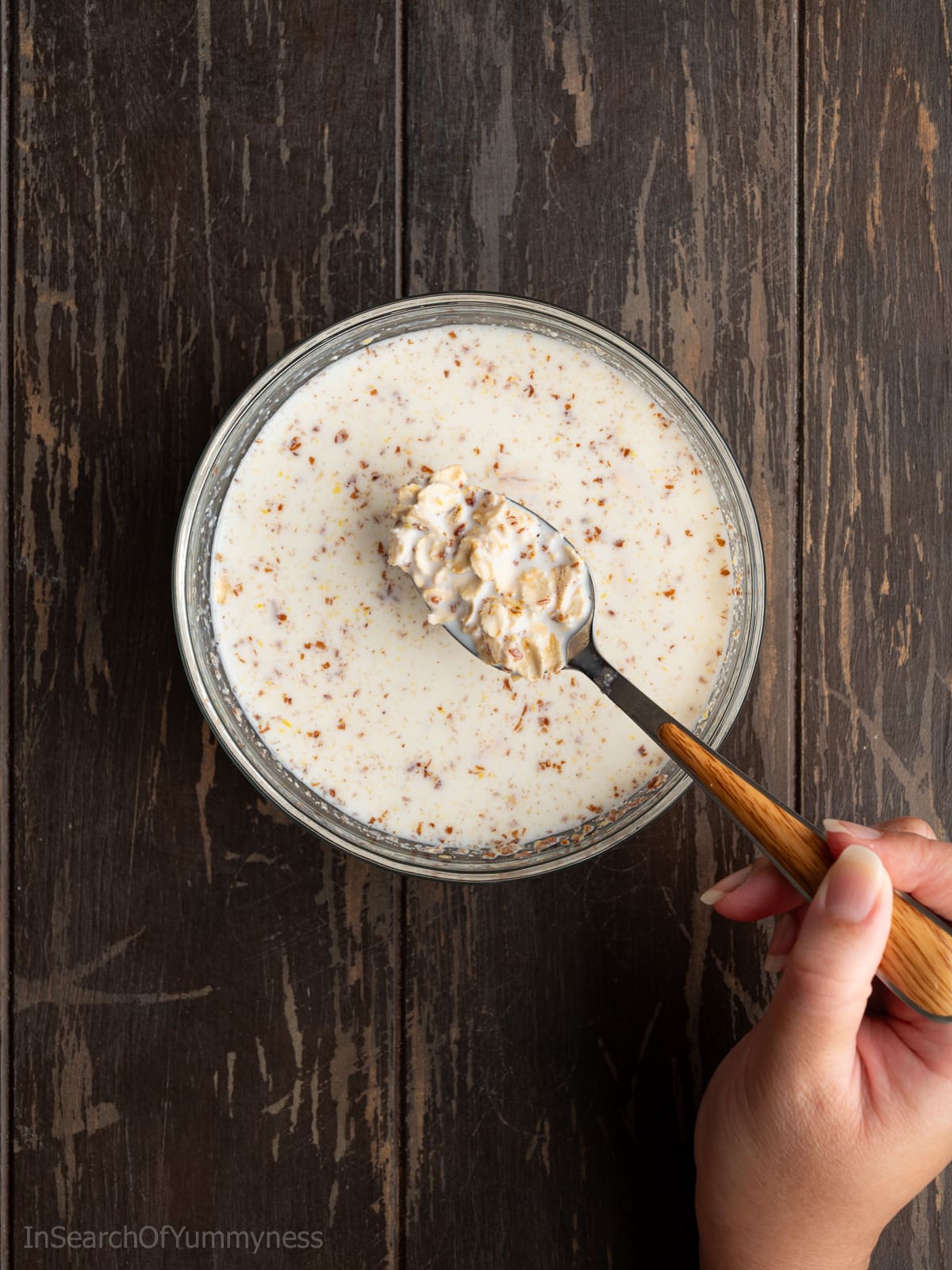 Soaking the raw rolled oats and the ground flaxseed in milk in a small bowl. Someone is using a spoon to lift out some of the oats and flaxseed to show the texture.