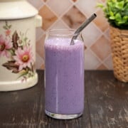 A tall glass filled with vibrant purple blueberry oat smoothie, with a metal straw inside the glass.