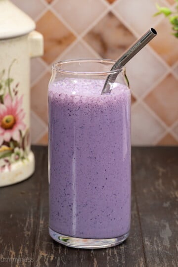 A tall glass filled with vibrant purple blueberry oat smoothie, with a metal straw inside the glass.