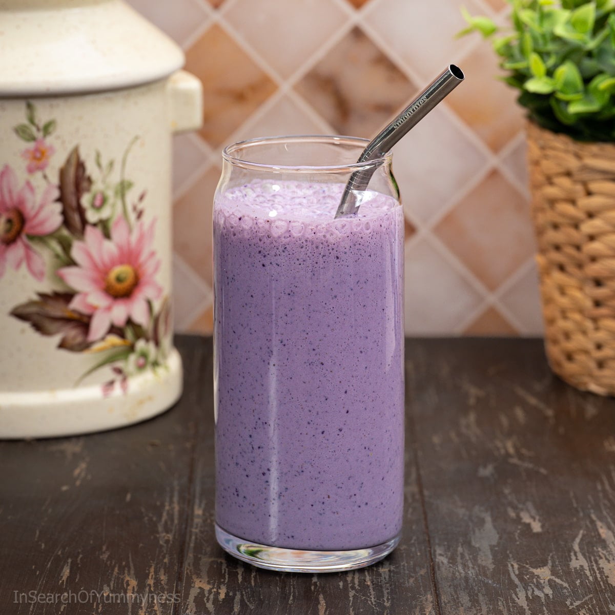 A tall glass filled with vibrant purple blueberry oat smoothie, with a metal straw inside the glass.