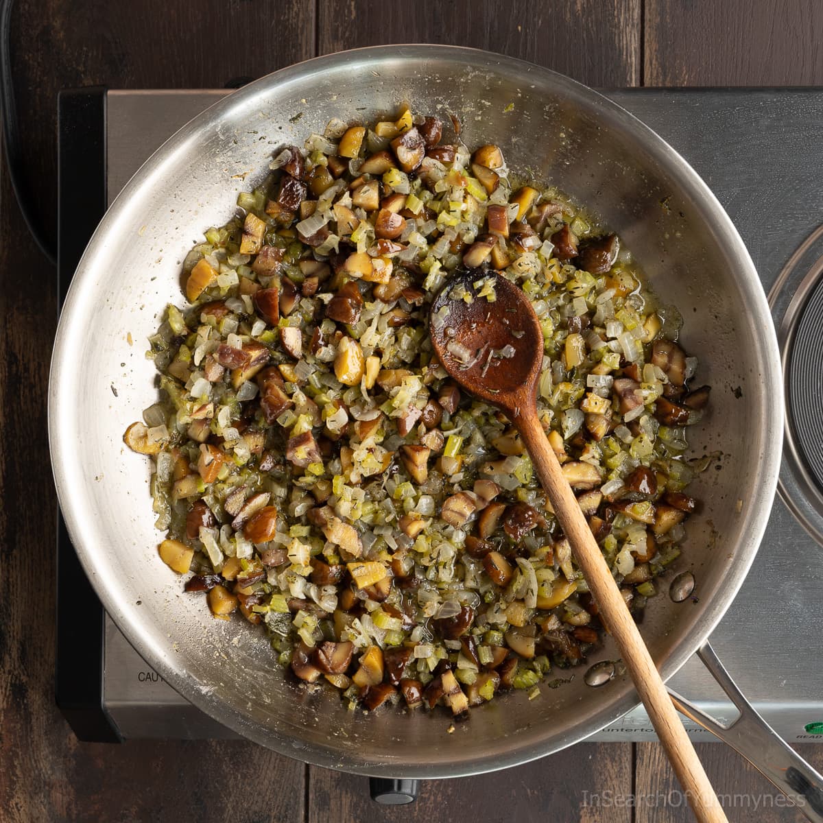 Cooked finely chopped onions, celery, chestnuts and herbs in a stainless steel skillet, with a wooden spoon.