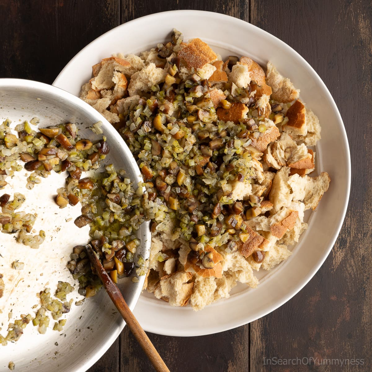 Adding the cooked vegetable mixture to the dry bread in a large white bowl.