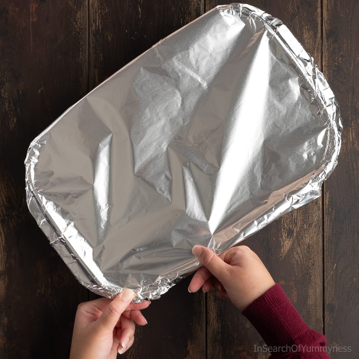 Someone crimping down the edges of aluminum foil over the top of the baking dish.