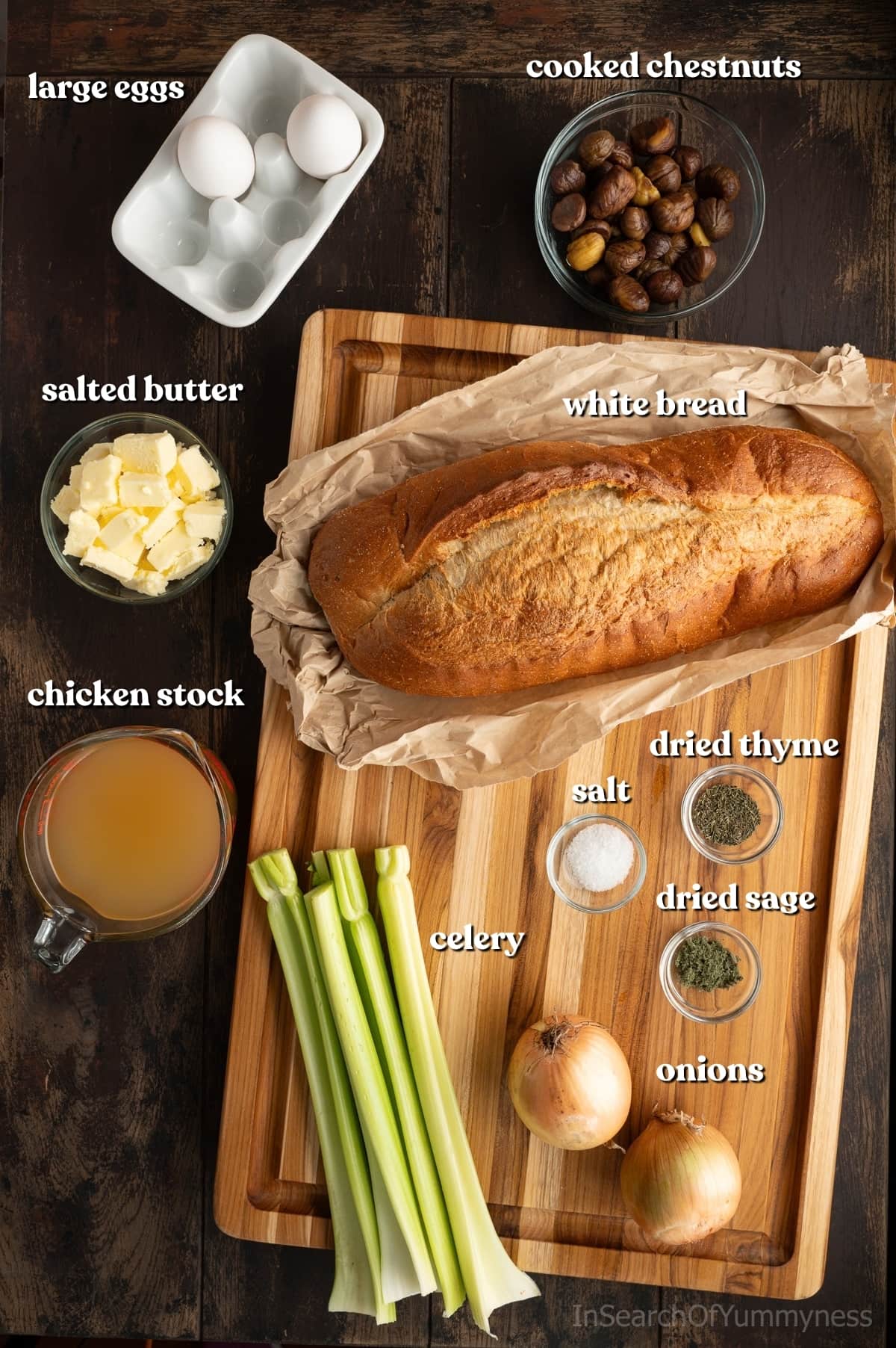 Ingredients for chestnut stuffing including a loaf of white bread, chicken stock, cooked chestnuts, eggs, butter, celery, onions, and seasonings on a wooden table.