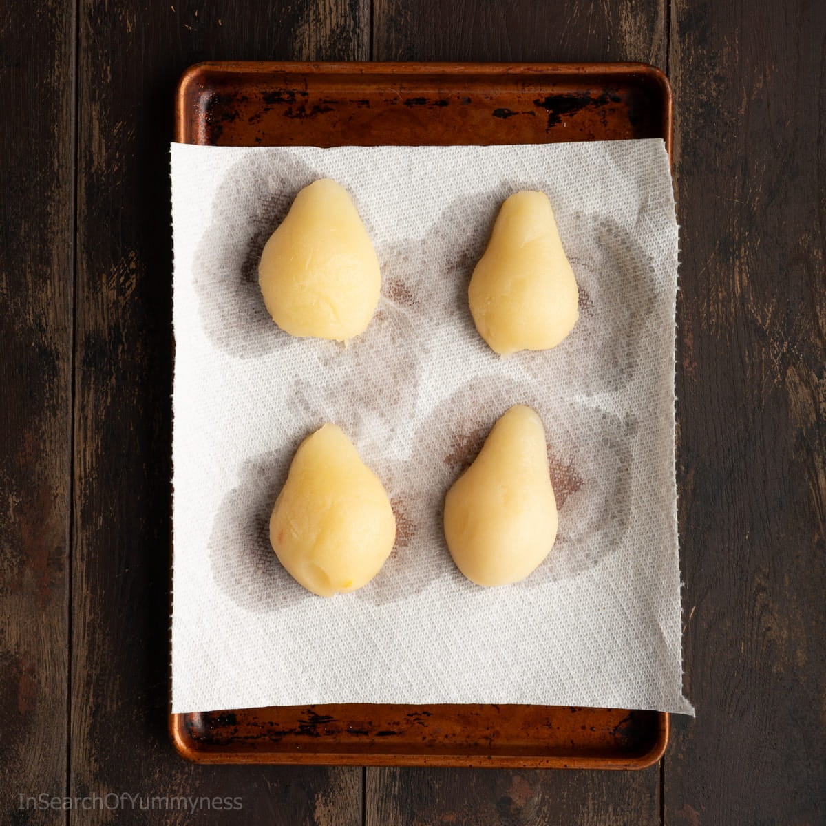 Four canned pear halves draining on a large piece of paper towel, which is sitting on a brown sheet pan.