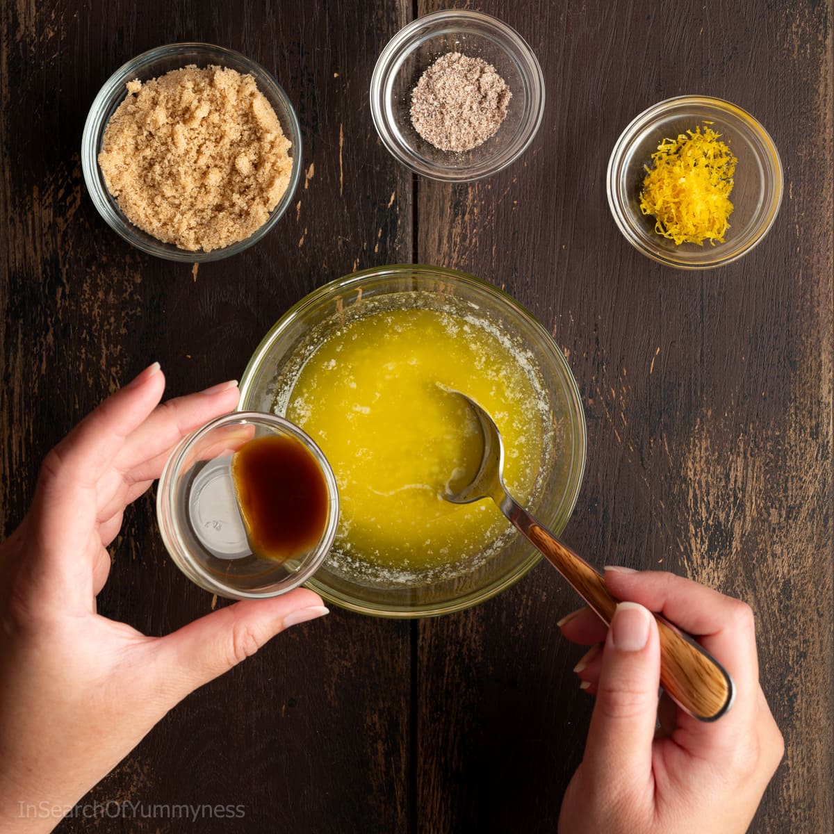 Adding vanilla extract to a clear bowl of melted butter, with other ingredients in smaller clear bowls around it.