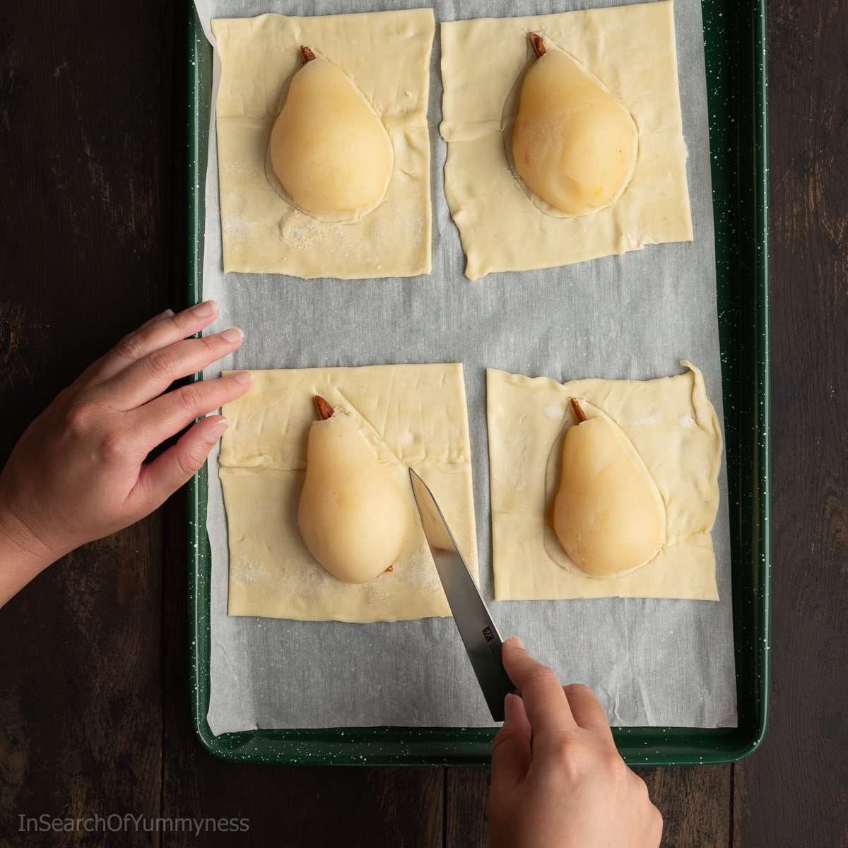 Someone using a knife to score the puff pastry around a pear half.