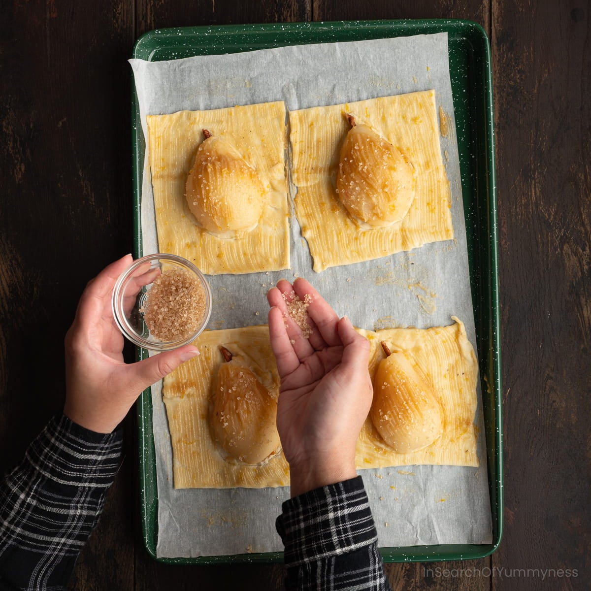 Someone sprinkling coarse turbinado sugar onto four unbaked pears on puff pastry waiting to go into the oven.