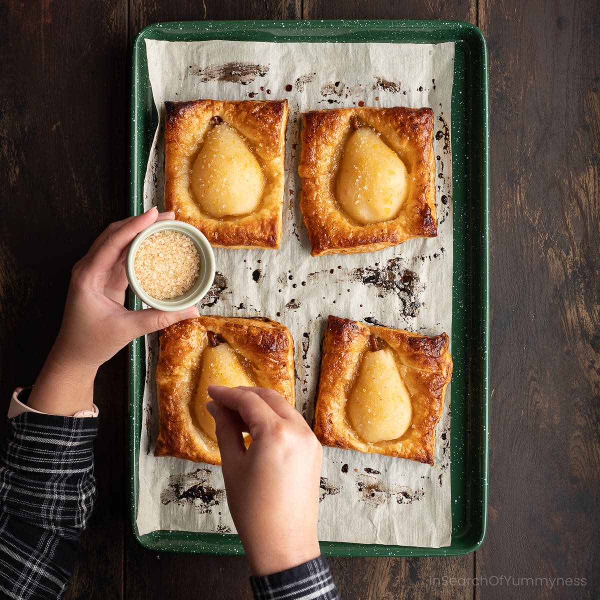 Someone sprinkling coarse turbinado sugar onto four baked pears in puff pastry.
