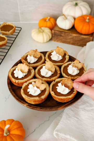 Several individual mini pumpkin pies decorated with whipped cream and pie dough cut-out shapes.