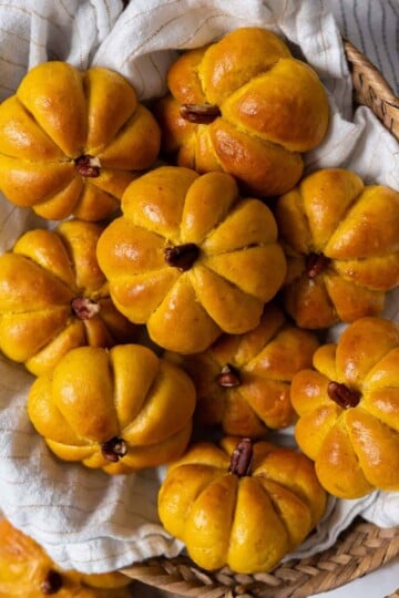 A bread basket full of cute pumpkin-shaped dinner rolls with a pecan stem.