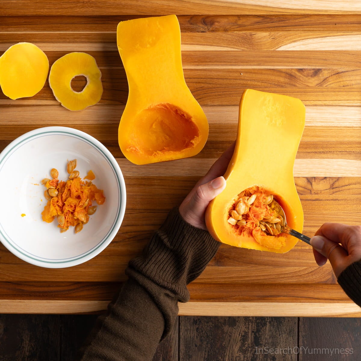 Someone using a spoon to scoop the seeds out of a halved butternut squash.