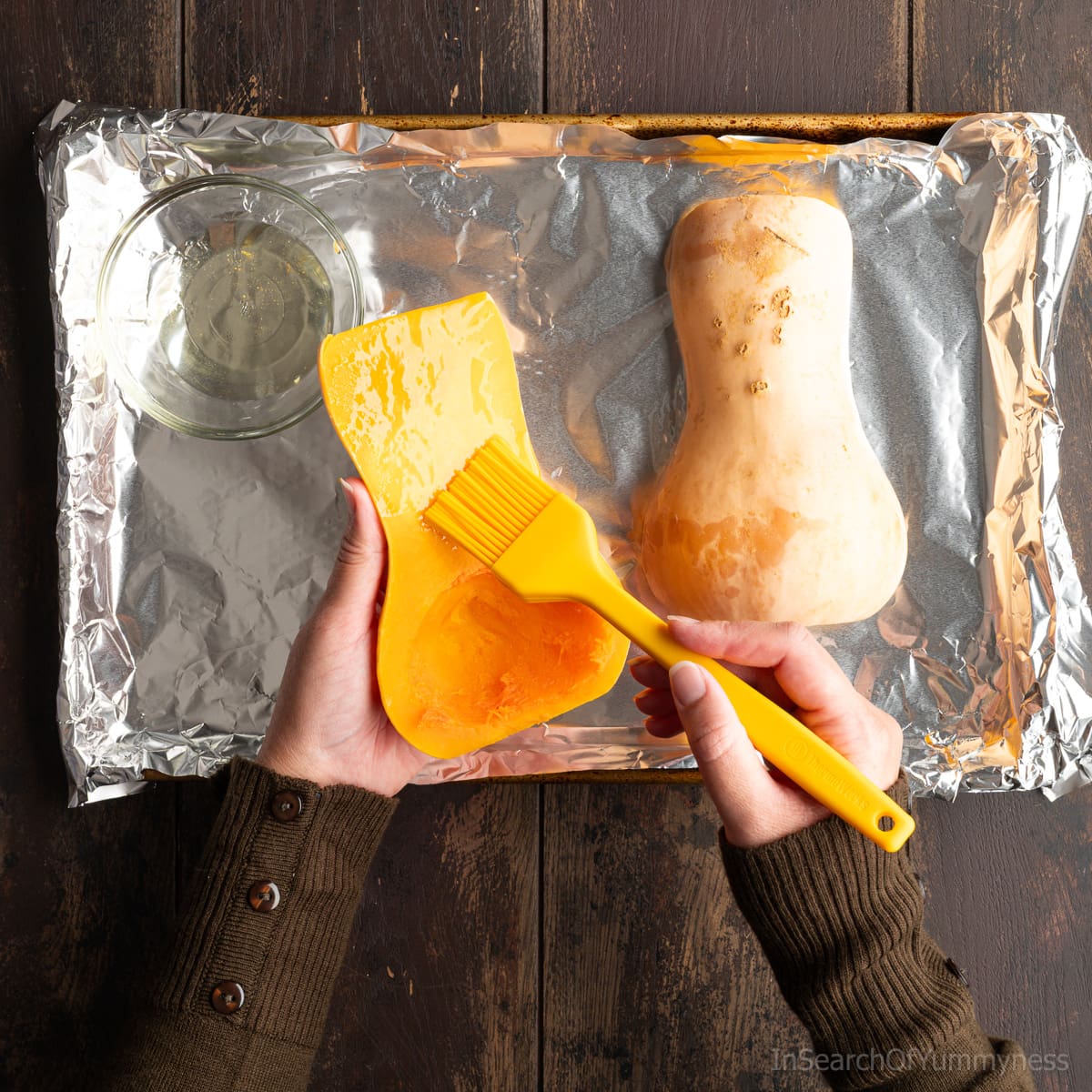 Someone brushing oil onto the inside of a halved butternut squash with a yellow silicone pastry brush.