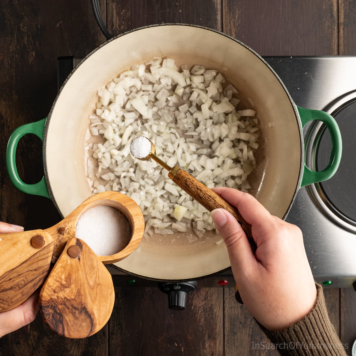 Someone adding salt to a green Le Creuset Dutch oven from a wooden salt cellar.
