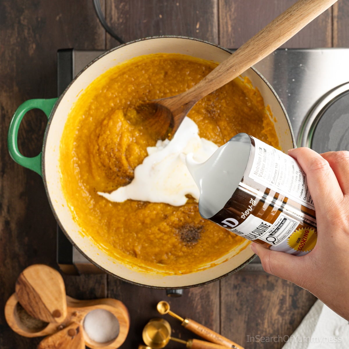Someone pouring coconut milk from a can into a green Dutch oven filled with curried butternut squash soup.