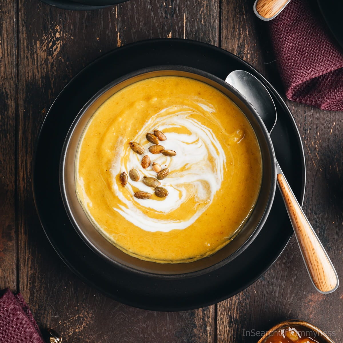 An overhead view of a vibrant yellow bowl of butternut squash soup garnished with pumpkin seeds and a swirl of coconut milk.