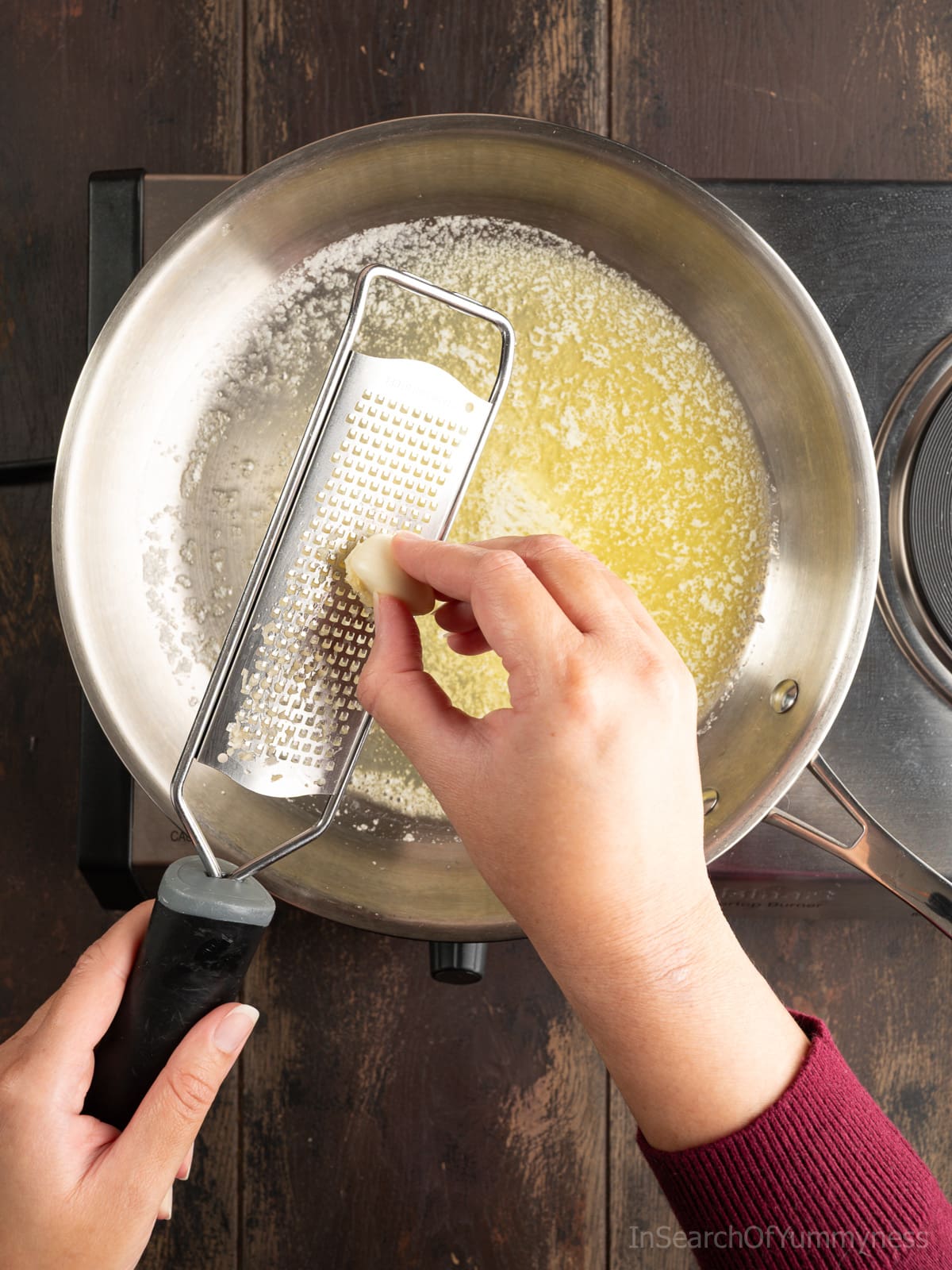Grating garlic on a Microplane rasp into a stainless steel skillet full of melted butter.