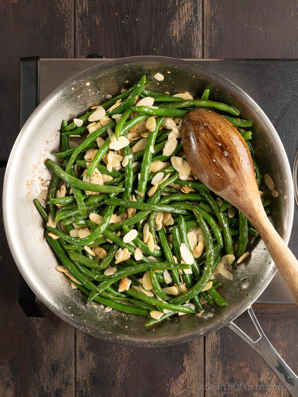 Buttery green beans sautéing in a large stainless steel skillet with minced garlic and slivered almonds.