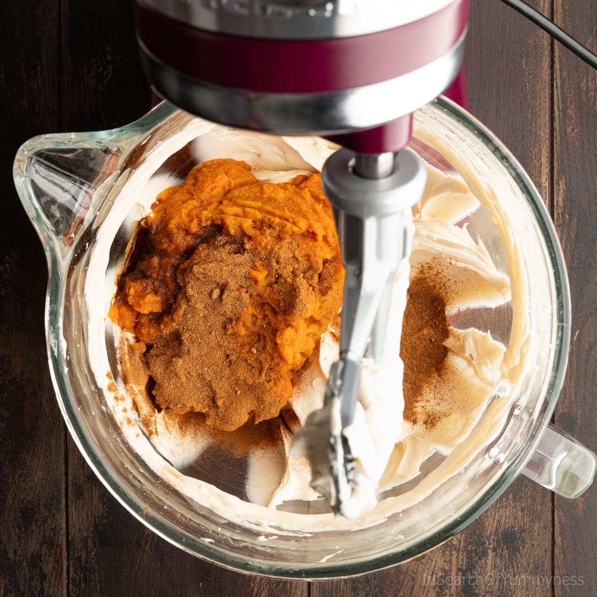 Pumpkin puree and spices added to the sugar and cream cheese in the mixing bowl of a KitchenAid stand mixer.