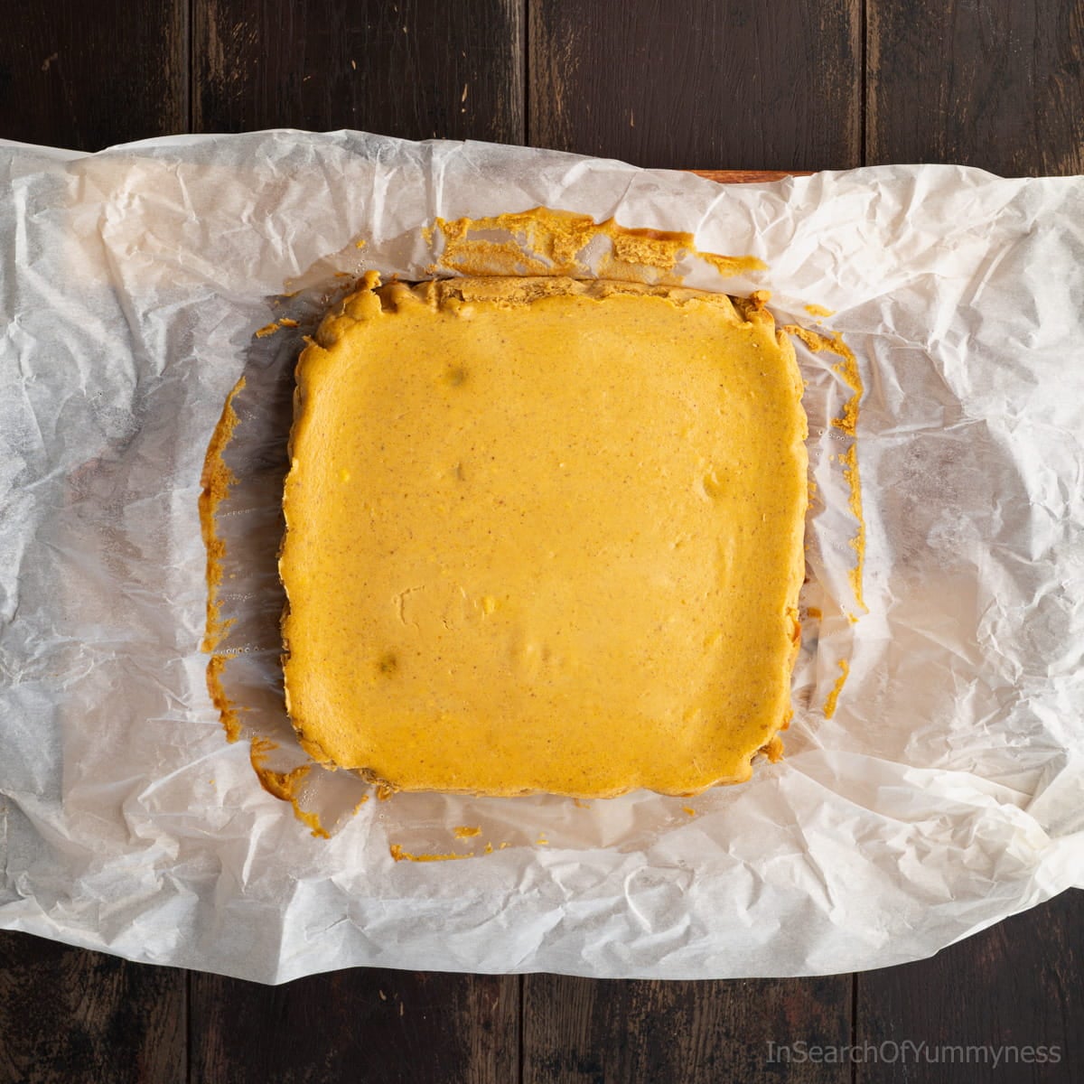 A baked slab of pumpkin cheesecake bars cooling on parchment paper after baking.