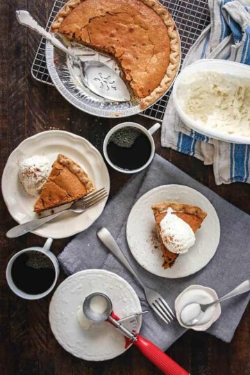 Slices of pumpkin chocolate chip pie on white plates next to two cups of coffee and a tub of ice cream, and the rest of the whole pie in the pie tin.