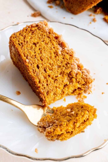 A slice of pumpkin coffee bake on a white plate with gold trim. There is a piece of the cake on a gold fork as well.